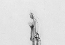 Un homme tout petit se tient au pied de la Statue Notre-Dame-du-Saguenay.