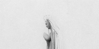Un homme tout petit se tient au pied de la Statue Notre-Dame-du-Saguenay.